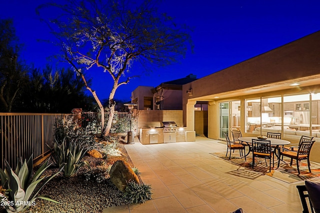 patio at twilight with a grill, a fenced backyard, outdoor dining area, and exterior kitchen