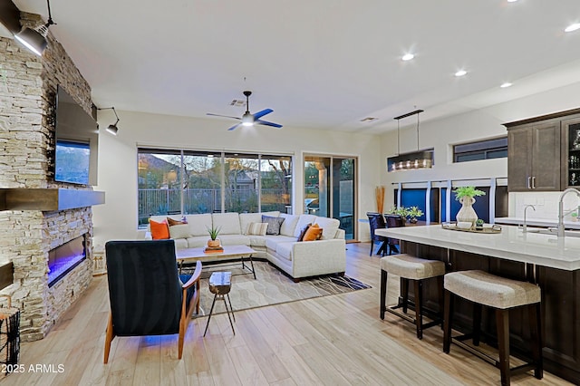 living room featuring recessed lighting, light wood finished floors, a stone fireplace, and a ceiling fan