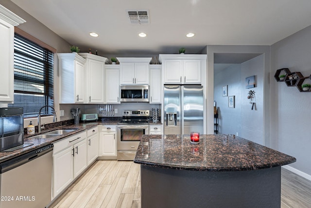 kitchen with dark stone counters, sink, appliances with stainless steel finishes, a kitchen island, and white cabinetry