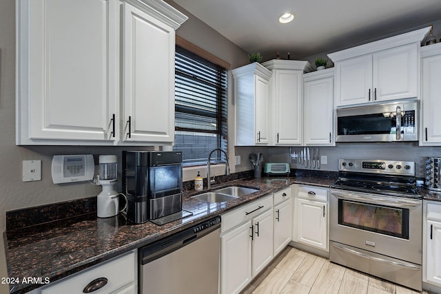 kitchen featuring white cabinets, appliances with stainless steel finishes, dark stone counters, and sink