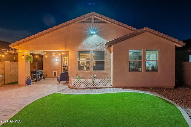 back house at twilight featuring a lawn and a patio area