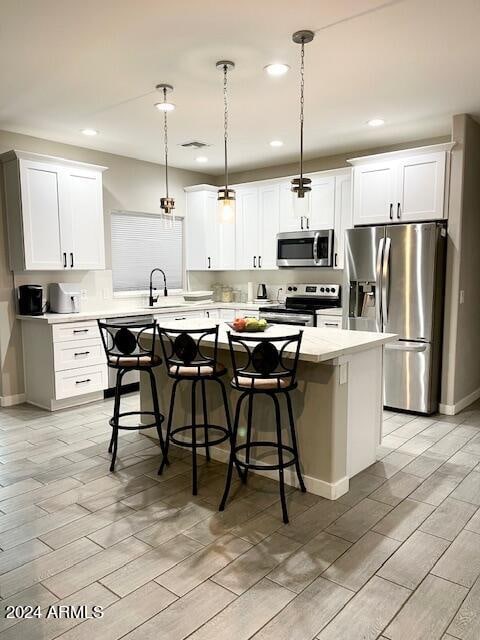 kitchen with appliances with stainless steel finishes, a center island, white cabinetry, and decorative light fixtures