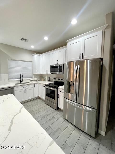 kitchen with sink, stainless steel appliances, white cabinetry, and light stone countertops