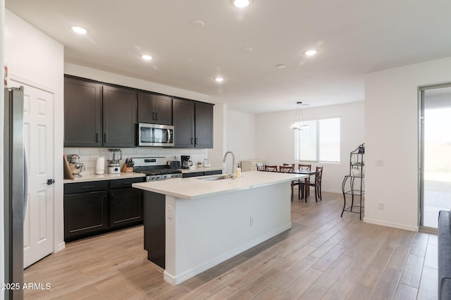 kitchen featuring stainless steel appliances, light hardwood / wood-style floors, sink, and hanging light fixtures