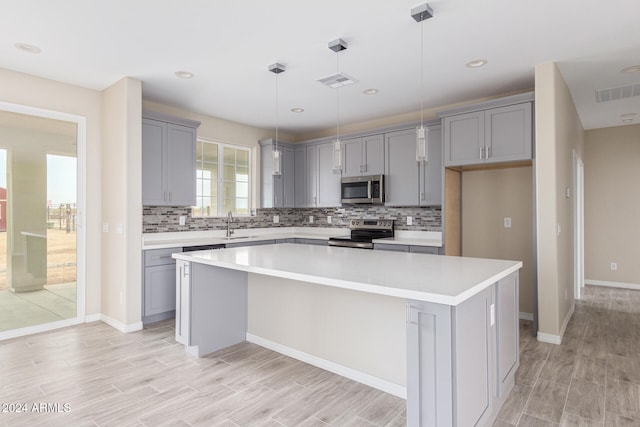 kitchen with light wood-type flooring, decorative light fixtures, appliances with stainless steel finishes, and a center island