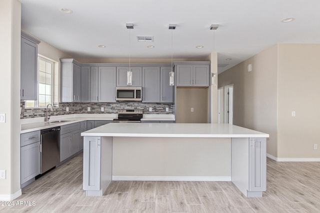 kitchen featuring sink, appliances with stainless steel finishes, light hardwood / wood-style flooring, a center island, and pendant lighting