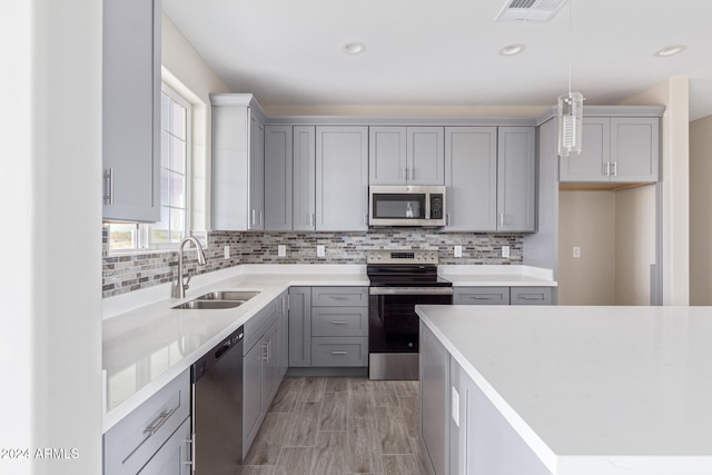 kitchen featuring appliances with stainless steel finishes, hanging light fixtures, sink, and gray cabinetry