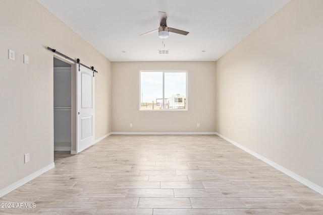 unfurnished bedroom featuring light wood-type flooring, a barn door, and ceiling fan