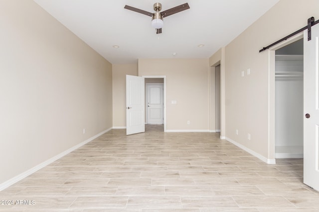 unfurnished bedroom with a barn door, ceiling fan, a closet, and light hardwood / wood-style flooring