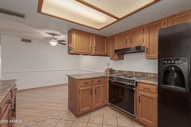 kitchen featuring visible vents, a textured ceiling, range with electric cooktop, under cabinet range hood, and black fridge