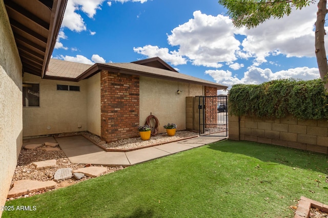 exterior space with brick siding, a yard, stucco siding, a gate, and fence