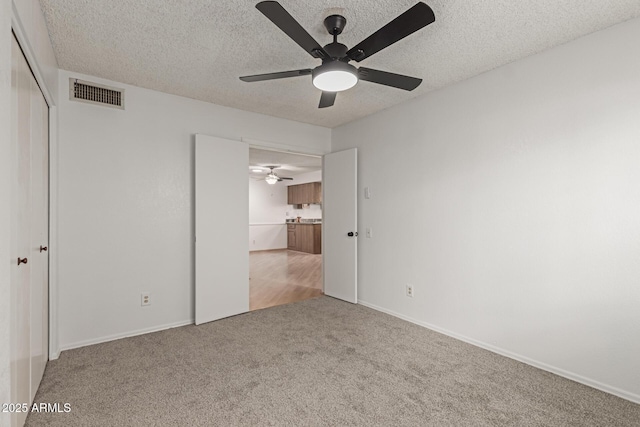 unfurnished bedroom featuring a textured ceiling, visible vents, a closet, and light colored carpet