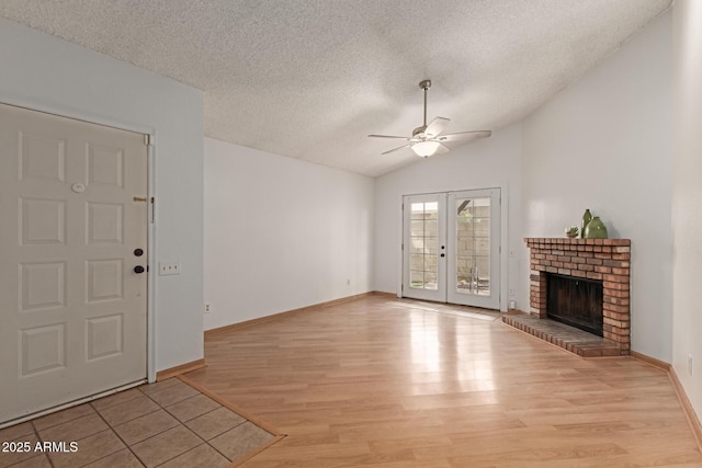 unfurnished living room featuring light wood finished floors, a ceiling fan, lofted ceiling, a textured ceiling, and a brick fireplace