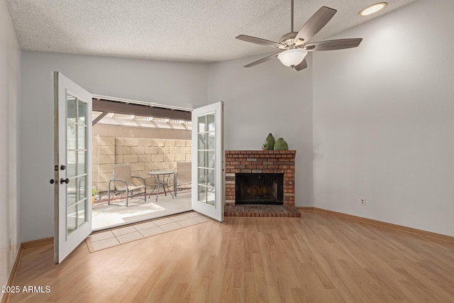 unfurnished living room with french doors, a fireplace, a textured ceiling, wood finished floors, and baseboards