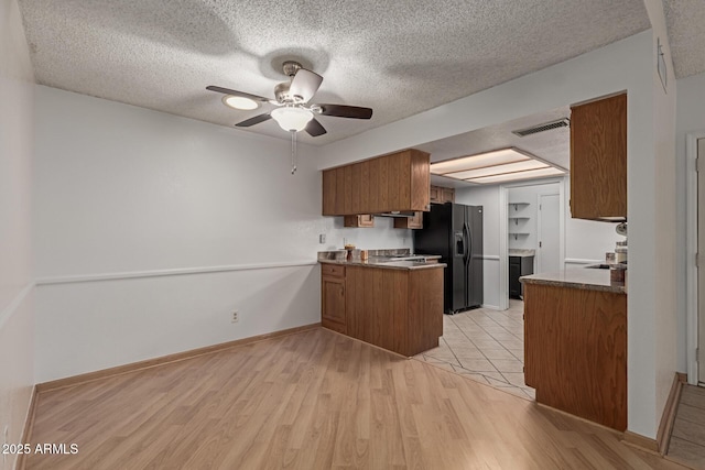 kitchen with light wood finished floors, visible vents, black fridge with ice dispenser, brown cabinets, and a peninsula