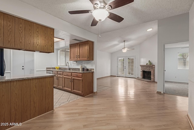 kitchen with lofted ceiling, brown cabinetry, a brick fireplace, a sink, and a textured ceiling