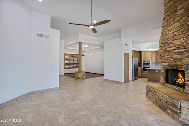 unfurnished living room featuring ceiling fan with notable chandelier and a stone fireplace