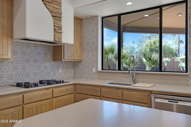 kitchen featuring wall chimney range hood, backsplash, stainless steel dishwasher, and sink