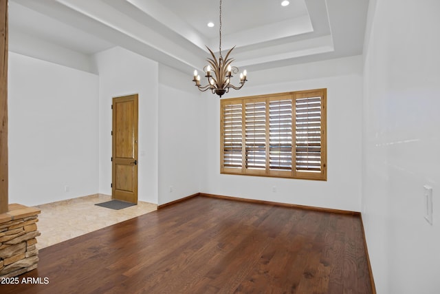 unfurnished room featuring hardwood / wood-style floors, a notable chandelier, and a tray ceiling