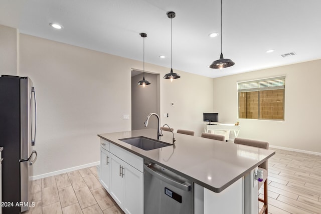 kitchen featuring appliances with stainless steel finishes, a kitchen island with sink, sink, pendant lighting, and white cabinets