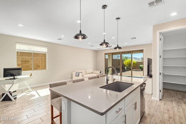 kitchen with sink, decorative light fixtures, light hardwood / wood-style flooring, white cabinetry, and an island with sink