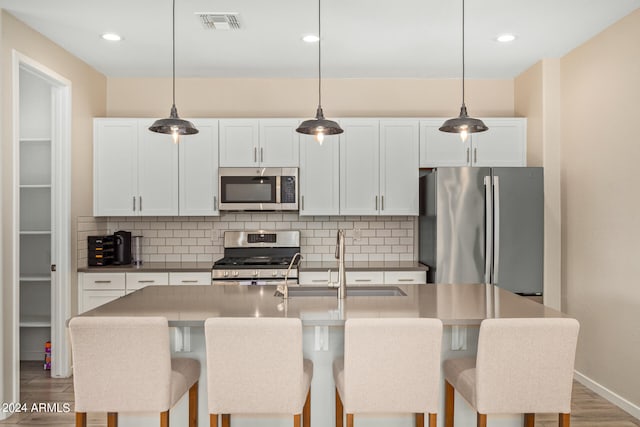 kitchen featuring tasteful backsplash, a kitchen island with sink, decorative light fixtures, and appliances with stainless steel finishes