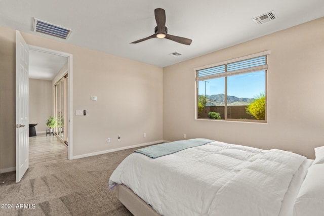 bedroom with a mountain view, ceiling fan, and light carpet