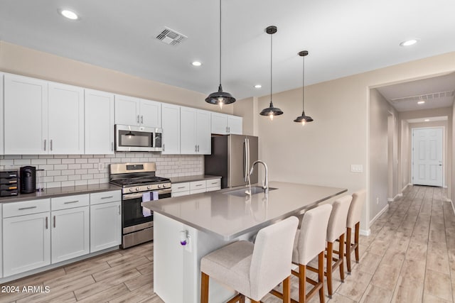 kitchen featuring white cabinets, sink, hanging light fixtures, appliances with stainless steel finishes, and light hardwood / wood-style floors