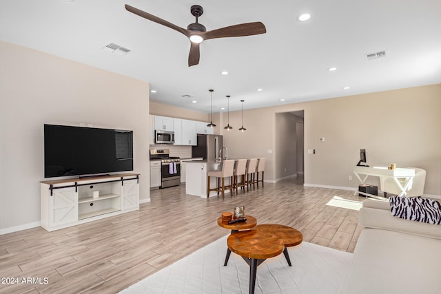 living room featuring ceiling fan, light hardwood / wood-style flooring, and sink