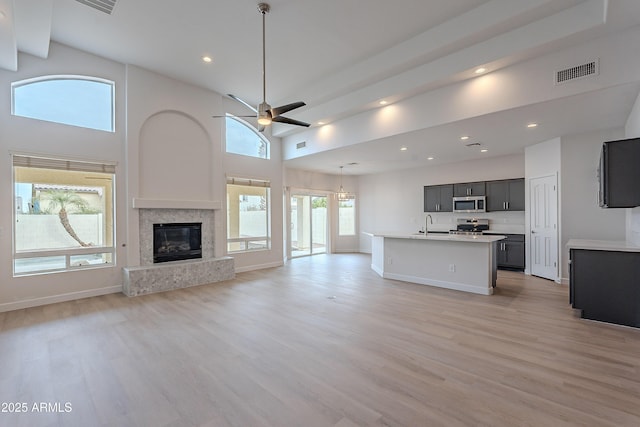 unfurnished living room featuring ceiling fan, sink, light hardwood / wood-style floors, and a high ceiling