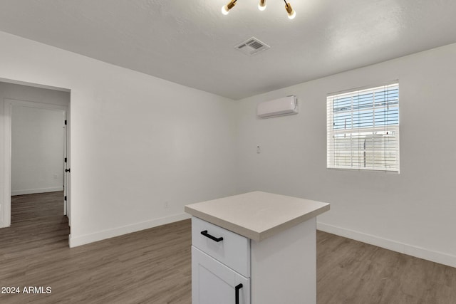 kitchen with a center island, an inviting chandelier, light hardwood / wood-style flooring, white cabinetry, and a wall unit AC