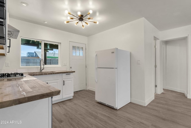 kitchen with white cabinets, white refrigerator, sink, light wood-type flooring, and a chandelier