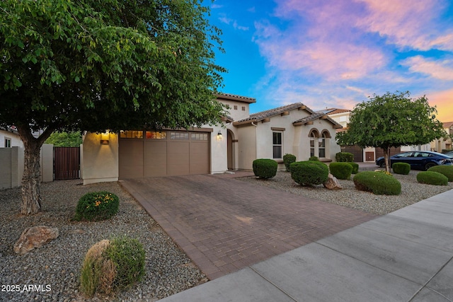 mediterranean / spanish-style home with a garage, decorative driveway, stucco siding, a gate, and a tile roof