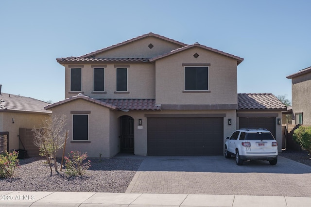 mediterranean / spanish house with decorative driveway, a tile roof, an attached garage, and stucco siding