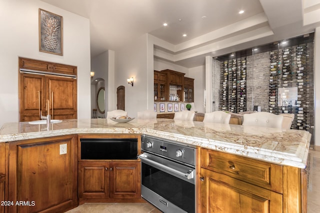 kitchen with paneled refrigerator, a warming drawer, light stone counters, brown cabinets, and oven