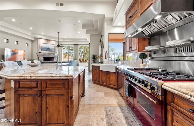 kitchen featuring visible vents, exhaust hood, a sink, brown cabinetry, and stainless steel appliances