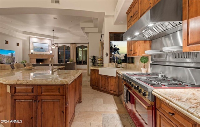 kitchen with range with two ovens, a center island with sink, sink, and extractor fan