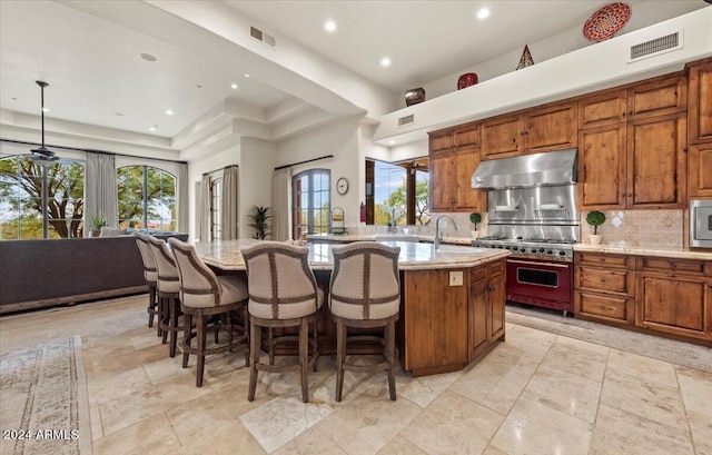 kitchen featuring appliances with stainless steel finishes, hanging light fixtures, tasteful backsplash, light stone countertops, and a center island with sink