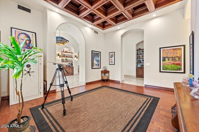 exercise area featuring visible vents, arched walkways, wood finished floors, a towering ceiling, and coffered ceiling