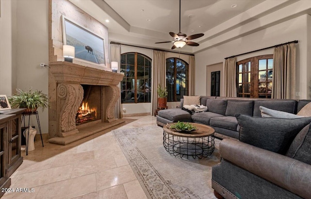 tiled living room with ceiling fan and a raised ceiling