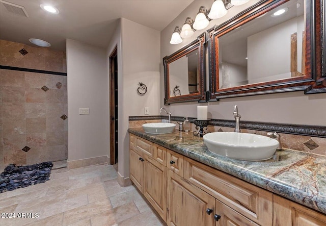 full bath with a sink, visible vents, a tile shower, and double vanity