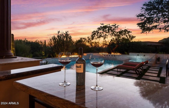 pool at dusk featuring a patio and an infinity pool