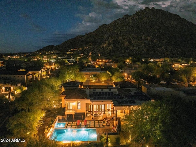 back of house at night featuring an outdoor pool and a mountain view