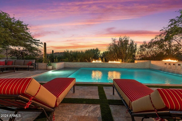 pool at dusk featuring an outdoor pool, a patio, an outdoor hangout area, and fence