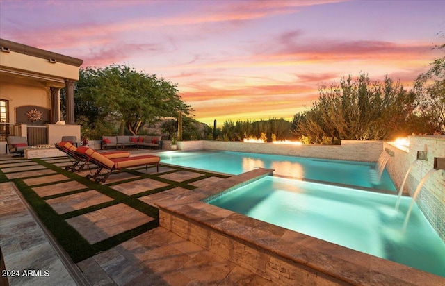 pool at dusk featuring a patio area, an outdoor living space with a fireplace, and a pool with connected hot tub