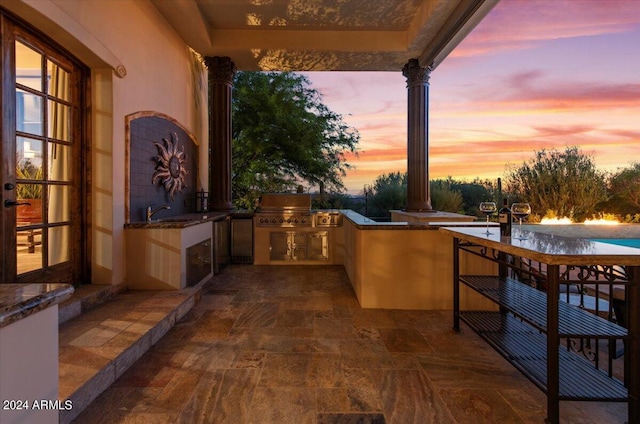 patio terrace at dusk featuring grilling area, a sink, and exterior kitchen