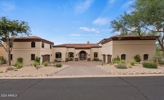 mediterranean / spanish house with a tile roof, curved driveway, and stucco siding