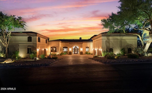 mediterranean / spanish-style home with a tile roof, stucco siding, and curved driveway