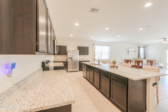 36467 W Pampoloma Ave, Maricopa, AZ 85138 - kitchen with stainless steel appliances, a sink, a kitchen breakfast bar, light tile patterned flooring, and dark brown cabinetry