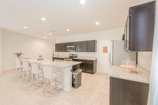36467 W Pampoloma Ave, Maricopa, AZ 85138 - kitchen with stainless steel appliances, a sink, a breakfast bar area, dark brown cabinetry, and light tile patterned floors
